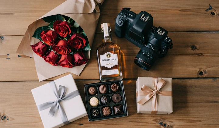 Appropriate gifts for meeting Slavic family: flowers, quality spirits, chocolates, and wrapped present arranged on wooden table